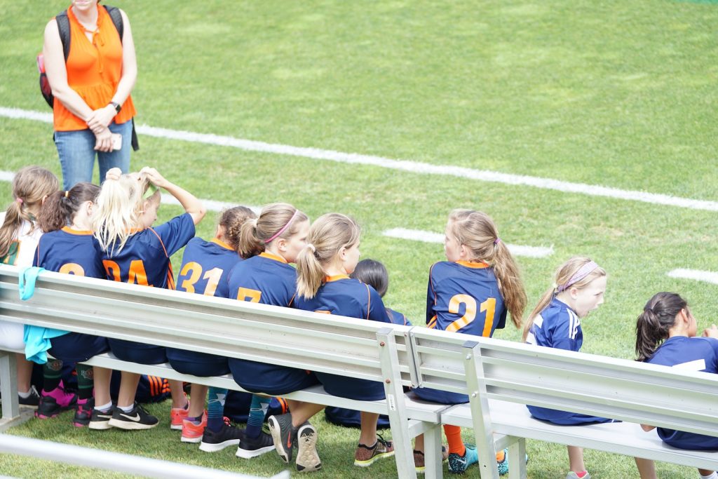 all girl football team sitting on white bench beside green field